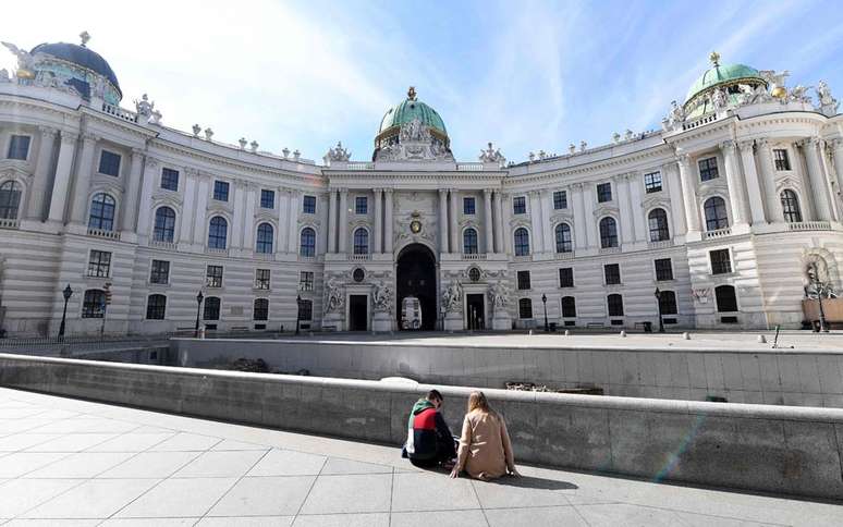 Em Viena, duas pessoas sentam em uma praça vazia. O governo austríaco proibiu reuniões de mais de cinco pessoas