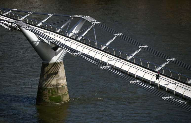 Uma mulher caminha pela Millennium Bridge, em Londres, que está vazia durante a hora do rush. O primeiro-ministro Boris Johnson orientou aos cidadãos britânicos que evitem atividades 'não essenciais' e contato interpessoal para conter o surto do coronavírus.