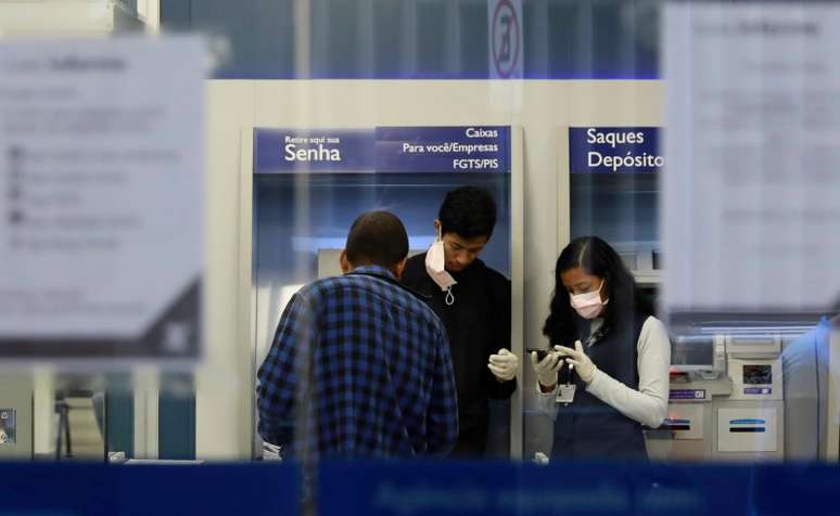 Funcionários de banco usando máscaras de proteção enquanto conversam com cliente, em meio à pandemia do coronavirus. 19/3/2020. REUTERS/Diego Vara 