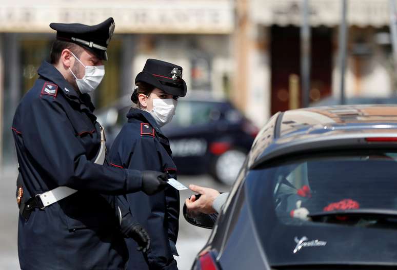 Policiais italianos usam máscara de proteção enquanto verificam se motorista tem razão válida para viajar durante bloqueio no país
21/03/2020
REUTERS/Yara Nardi