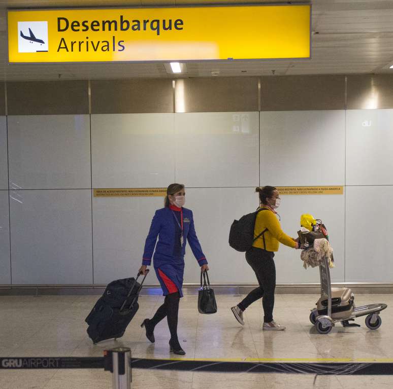 Passageira e tripulante desembarcam usando máscara no Terminal 3 do Aeroporto internacional de Guarulhos, na Grande São Paulo, em meio à epidemia do novo coronavírus. 