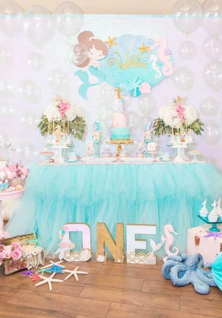 65. Mesa de festa infantil sereia decorada com babado azul ao redor da mesa e balões transparentes imitando bolhas d’água – Foto: Pinterest