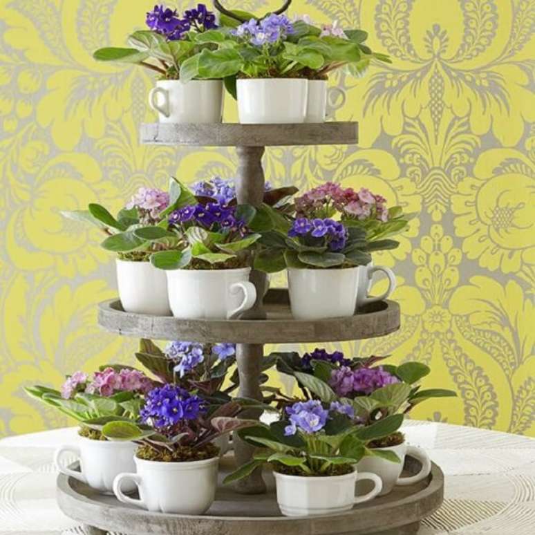 23- O arranjo para evento utiliza mudas de violetas plantadas em xícaras brancas. Fonte: Jeito de Casa