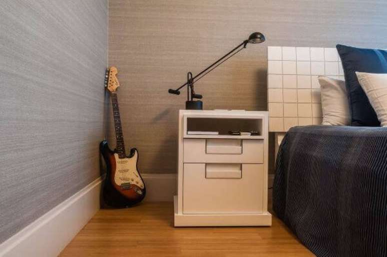 42. O criado mudo branco serve de apoio para a lumin&aacute;ria. Fonte: Maricy Marcos Borges