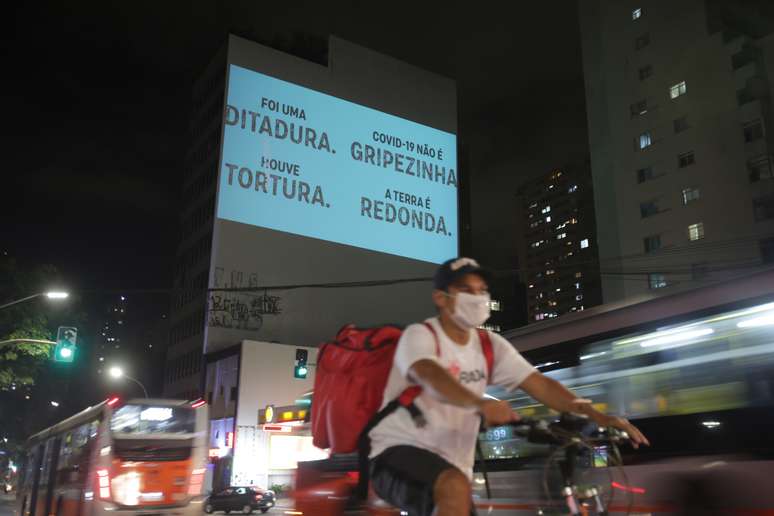 Entregador realiza o seu trabalho enquanto prédio estampa mensagem contra Bolsonaro