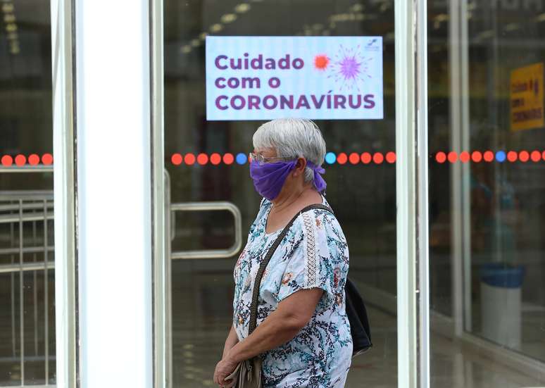 Idosa usa lenço como máscara de proteção contra o novo coronavírus enquanto passa por em agência bancária em Curitiba