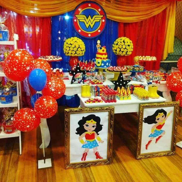 29. Linda decora&ccedil;&atilde;o de festa Mulher Maravilha com quadros grandes, arranjo de flores amarela e bal&otilde;es ao lado da mesa principal &ndash; Foto: Meninas Festeiras