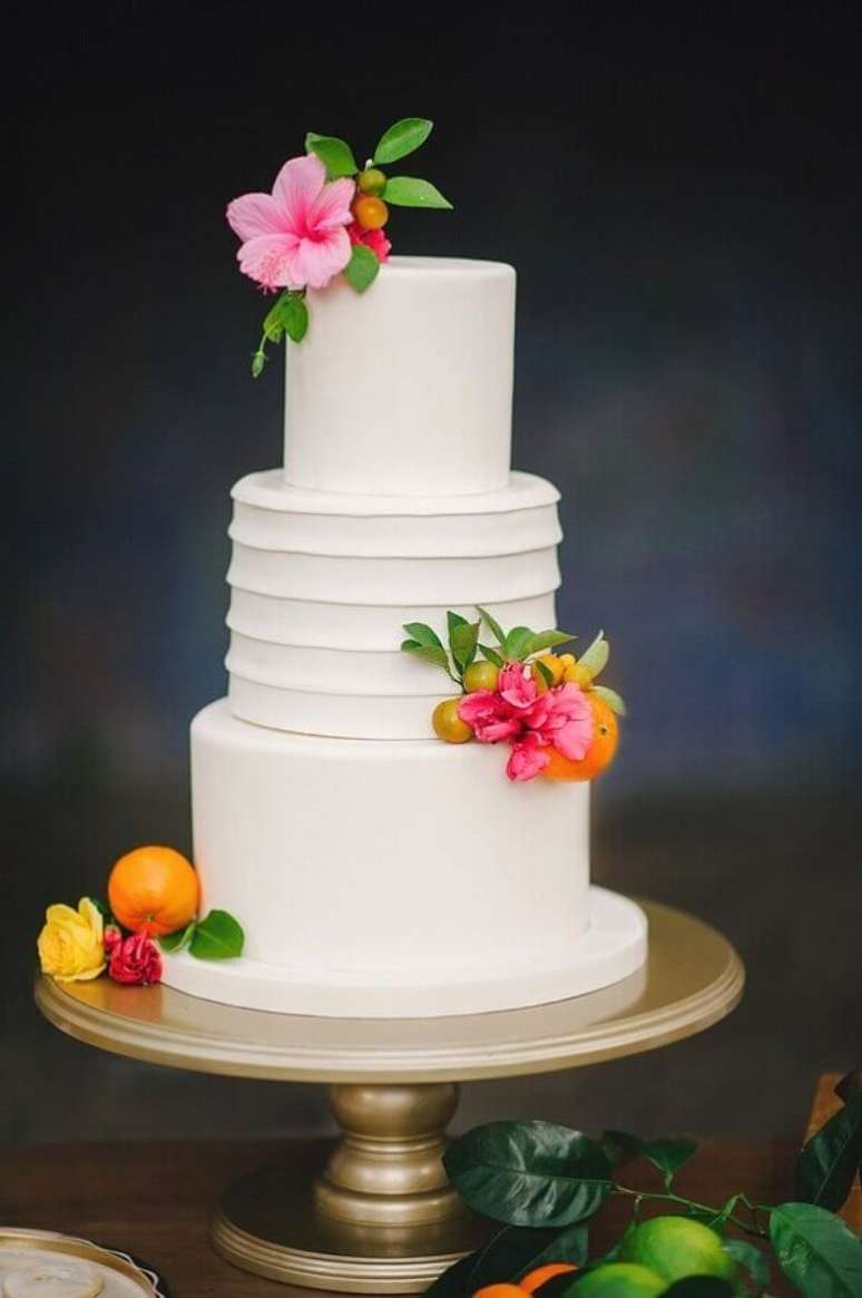 13. Bolo tropical para festa de casamento confeitado todo branco e decorado com flores bem coloridas para festa tropical – Foto: Brides