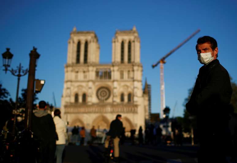 Homem com máscara de proteção passa pela frente da catedral de Notre-Dame de Paris, enquanto o sino tocava. 15/4/2020. REUTERS/Gonzalo Fuentes