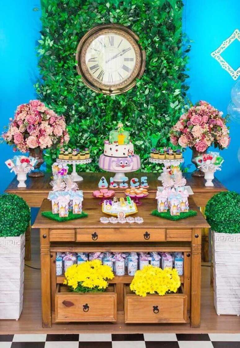 31. Decora&ccedil;&atilde;o de festa Alice no Pa&iacute;s das Maravilhas simples com mesa de madeira e painel de folhagens com rel&oacute;gio antigo &ndash; Foto: Pinterest