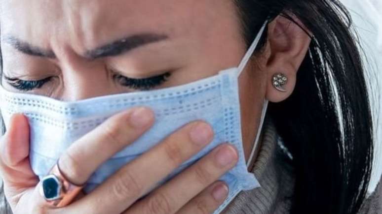 Mulher com m&aacute;scara e tossindo