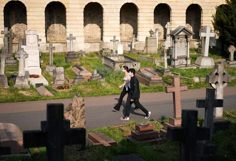 Pessoas usando máscaras de proteção andam no cemitério de Brompton,em Londres, em meio à pandemia de coronavírus. 24/4/2020. REUTERS/Henry Nicholls