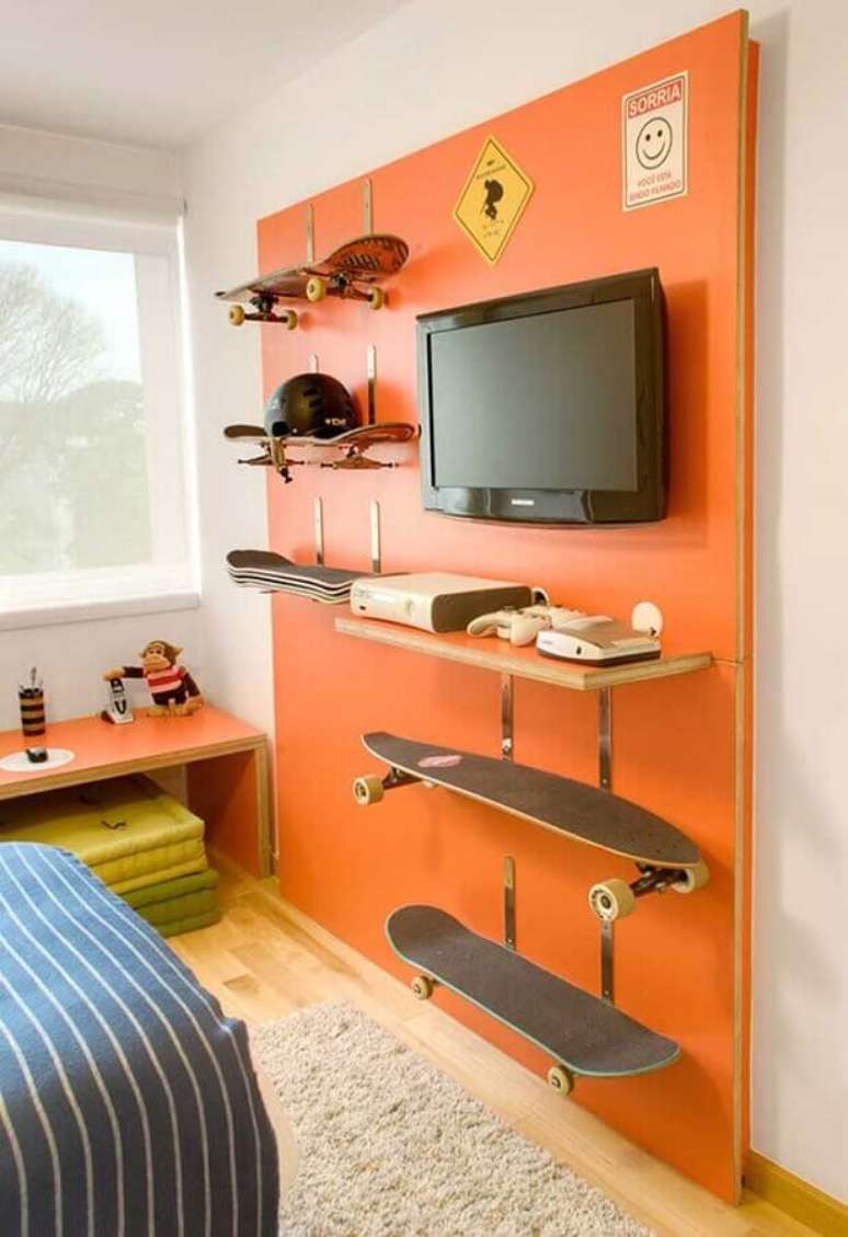 77. Quarto gamer decorado com painel laranja para TV e com suporte para apoiar skates – Foto: Pinterest