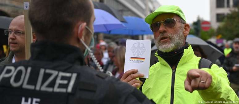 Homem mostra Constituição alemã a policial em protesto contra confinamento, em Frankfurt