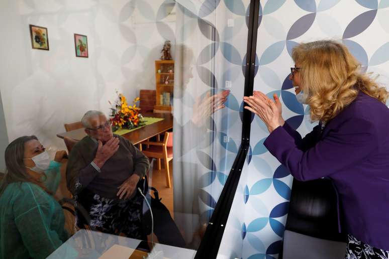 Mulher fala com o pai por meio de uma barreira de vidro em um asilo em Portugal, durante a pandemia do coronavírus. 12/5/2020. REUTERS/Rafael Marchante