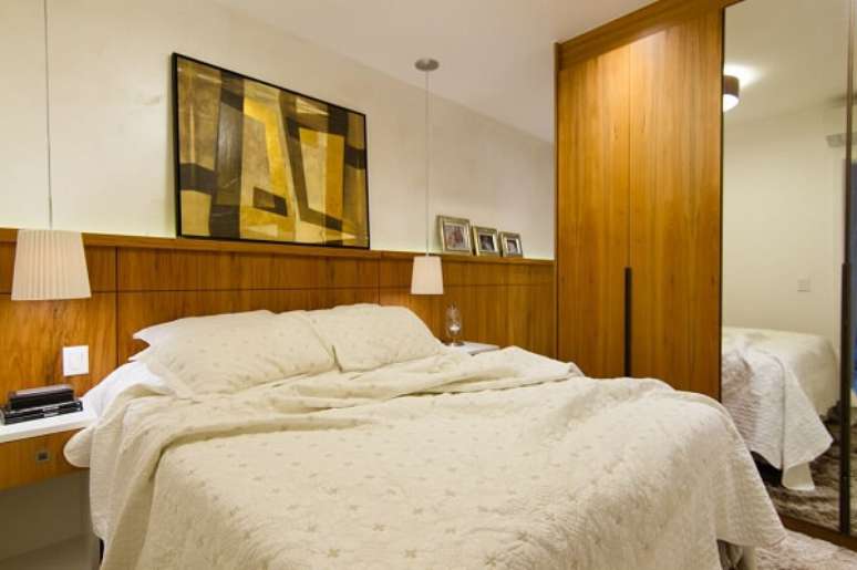 15. Cabeceira de madeira comum e lumin&aacute;rias brancas e guarda roupa casal mdf com porta de espelho. Projeto por Tektos
