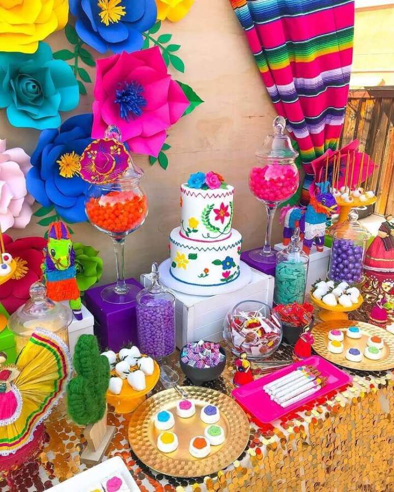 26. Decoração de mesa de festa mexicana super colorida com flores de papel no painel ao fundo – Foto: Sweet Tooth Candy Buffets