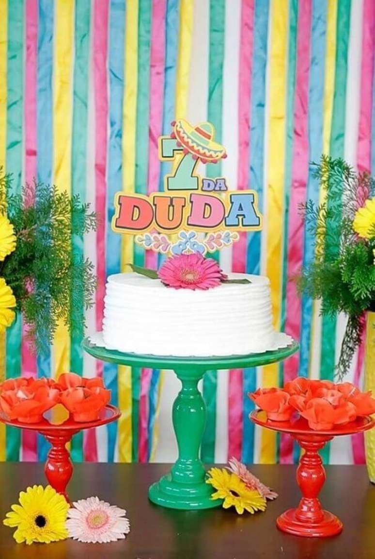 43. Painel com fitas coloridas para decoração de festa mexicana com bolo branco decorado com flor rosa – Foto: Pinterest