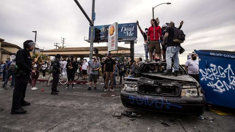 Manifestantes no topo de um carro da polícia queimado em Los Angeles, Califórnia
