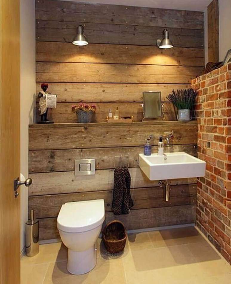 31. Banheiro rústico simples decorado com revestimento de madeira para parede e arandela metálica – Foto: Dicas Decor