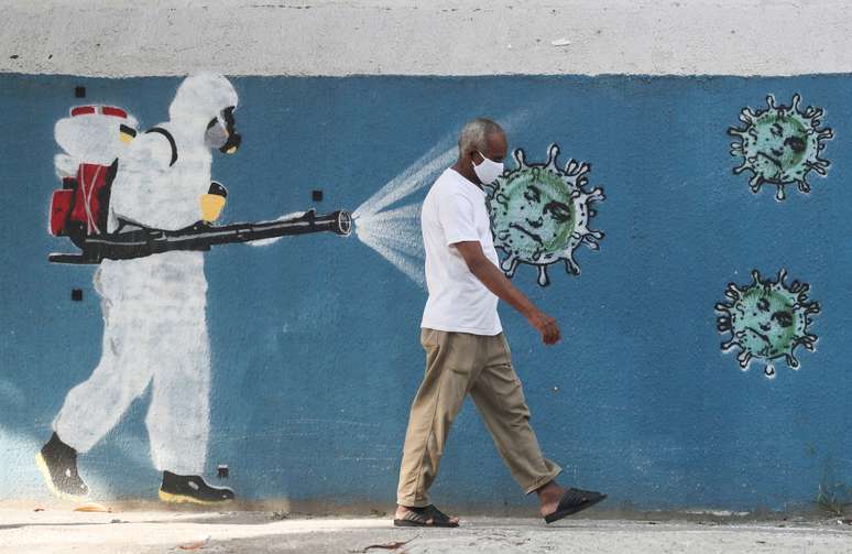 Homem passa pela frente de um grafite, enquanto um funcionário do serviço de saúde borrifa um spray contra o coronavírus. 12/6/2020. REUTERS/Sergio Moraes