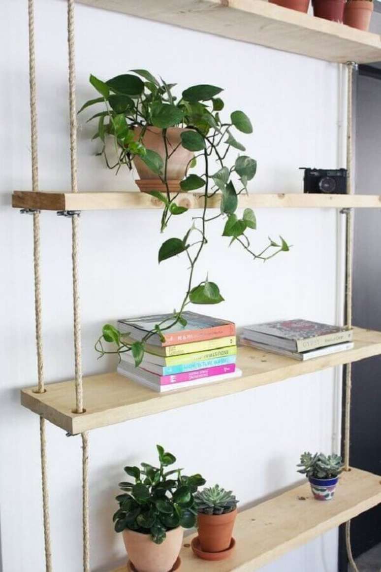 13. Prateleira de madeira suspensa por corda decorada com vasos de plantas e livros – Foto: Ligia Batschke
