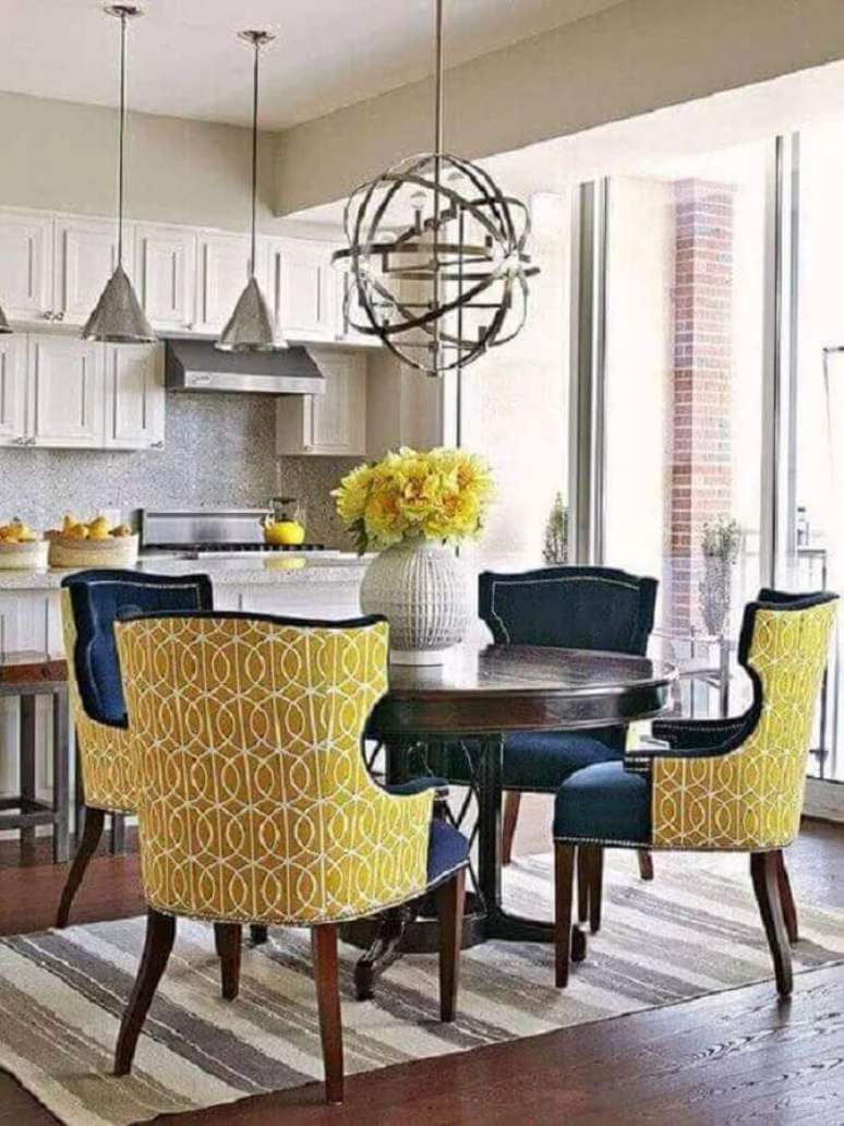 33. Sala de jantar clássica decorada com cadeiras azuis e amarelas e vaso para centro de mesa de jantar com arranjo de flores amarelas – Foto: Revista VD