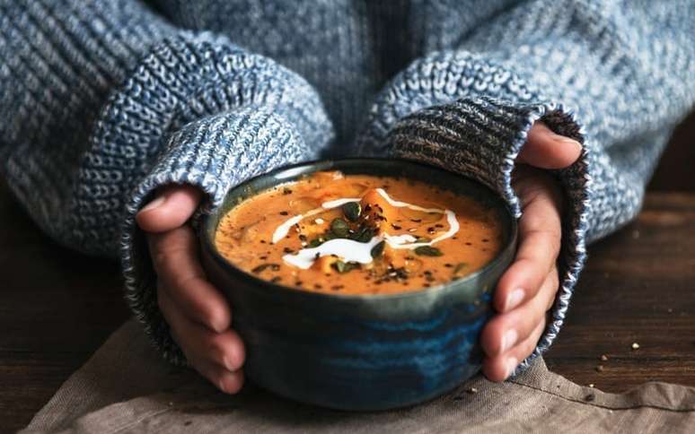 Mãos femininas segurando uma tigela de sopa de abóbora