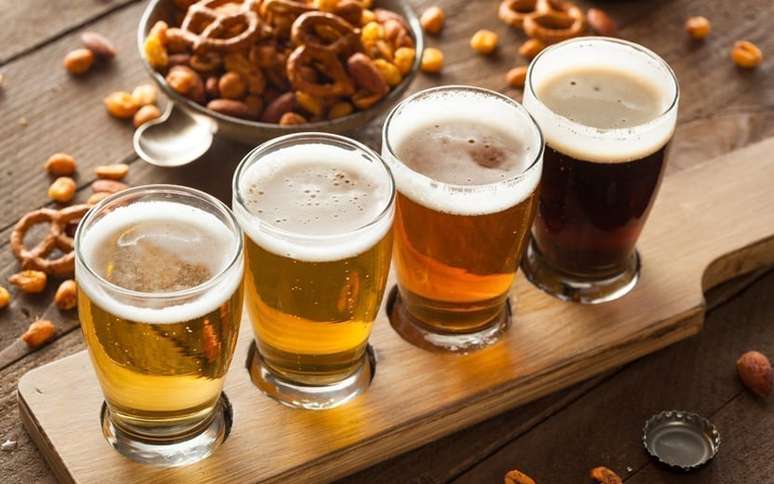 Tipos de cerveja sobre uma tábua com petisco atrás