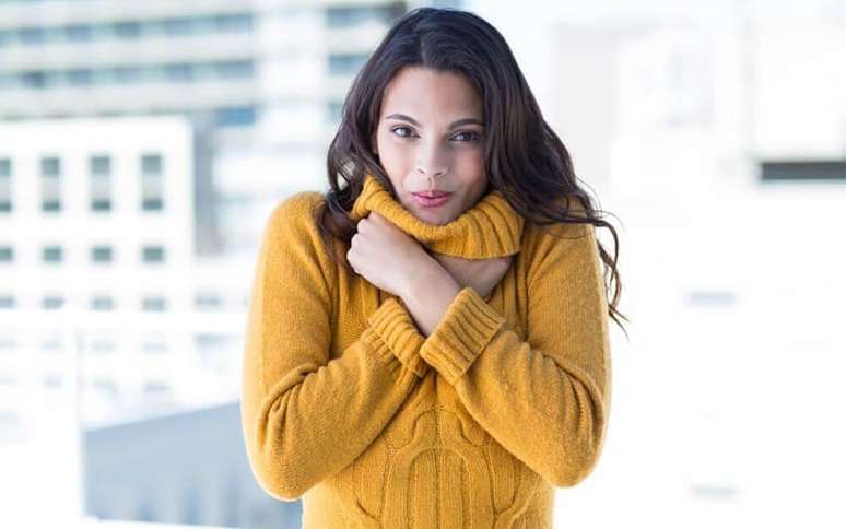 Mulher com roupa de lã, se abraçando de frio