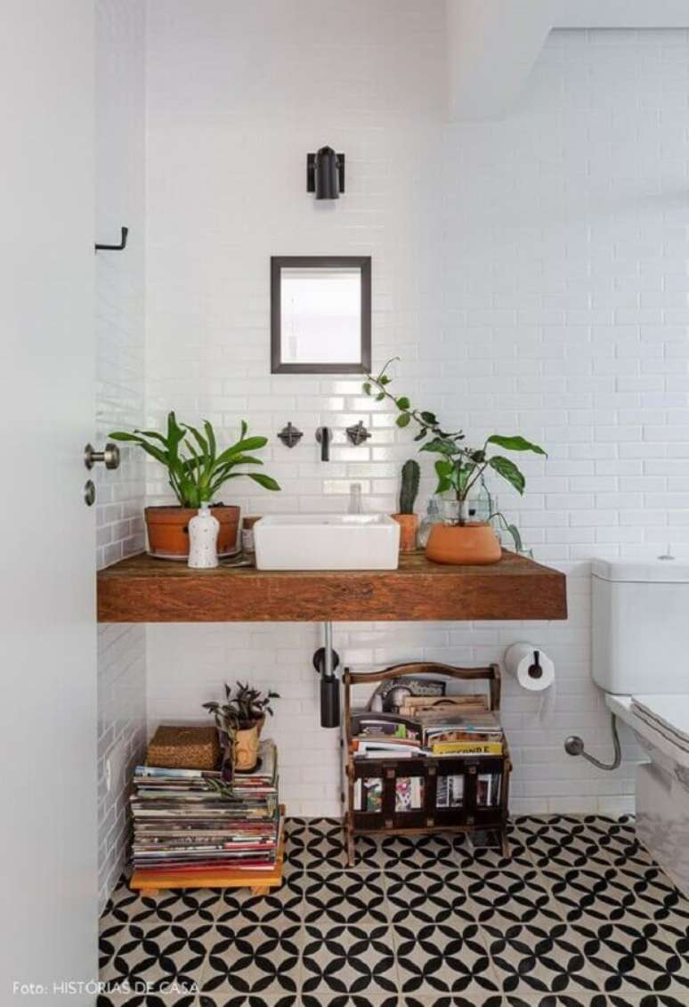 26. Decoração com plantas no banheiro simples com bancada de madeira e piso preto e branco – Foto: Histórias de Casa