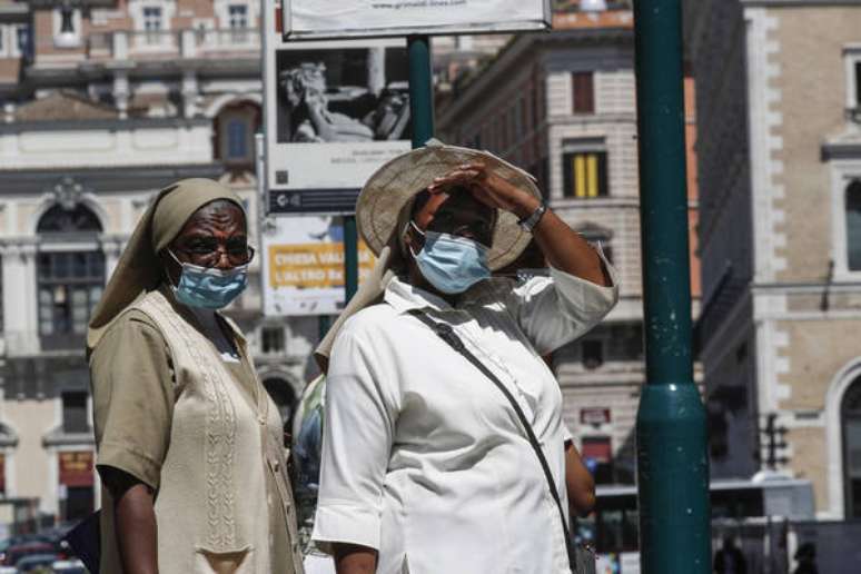 Pedestres se protegem do novo coronavírus e do sol em Roma, capital da Itália