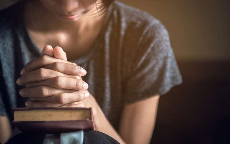 Mulher com as mãos fechadas, orando sobre uma bíblia