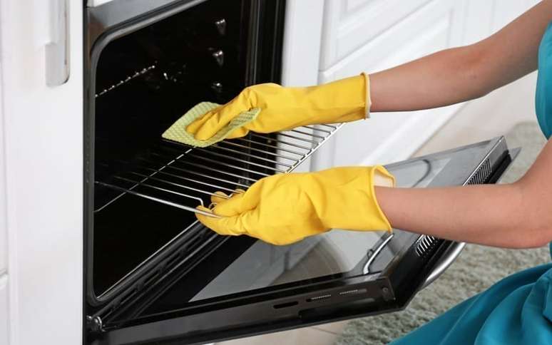 Pessoa limpando forno com pano e usando luvas amarelas