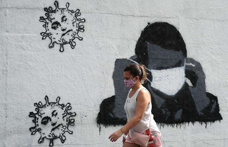 Mulher passa por grafite do presidente Jair Bolsonaro ajustando sua máscara protetora e em forma de vírus, em meio ao surto de Covid-19 no Rio de Janeiro. 02/07/2020. REUTERS/Sergio Moraes