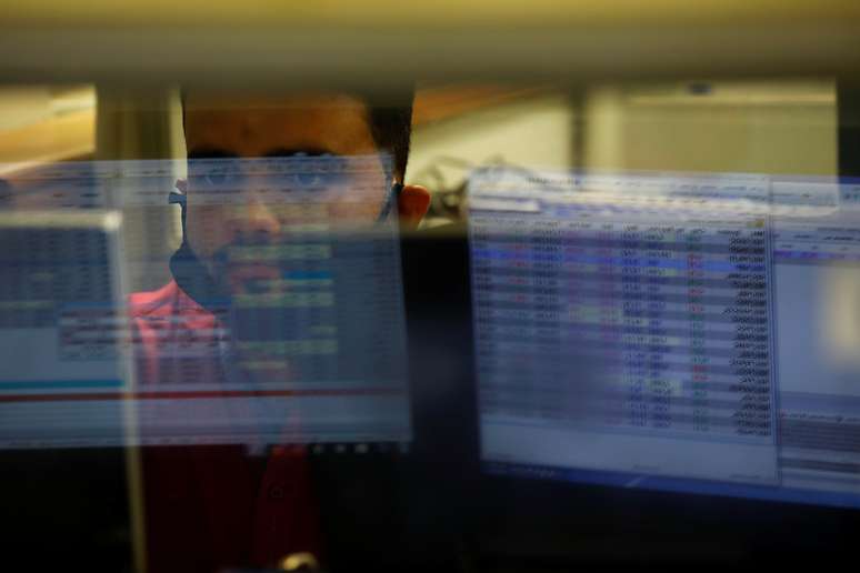 Telas de computadores refletidas num vidro, na frente do qual um operador de mercado financeiro trabalha. 30/6/2020. REUTERS/Akhtar Soomro