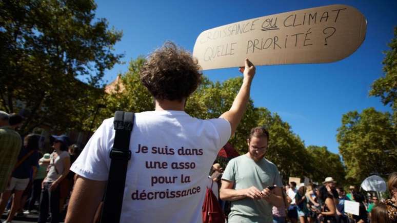 Manifestante protesta a favor do decrescimento na França em 2018, com cartaz em que se lê: ‘Crescimento ou clima, o que é prioridade?’