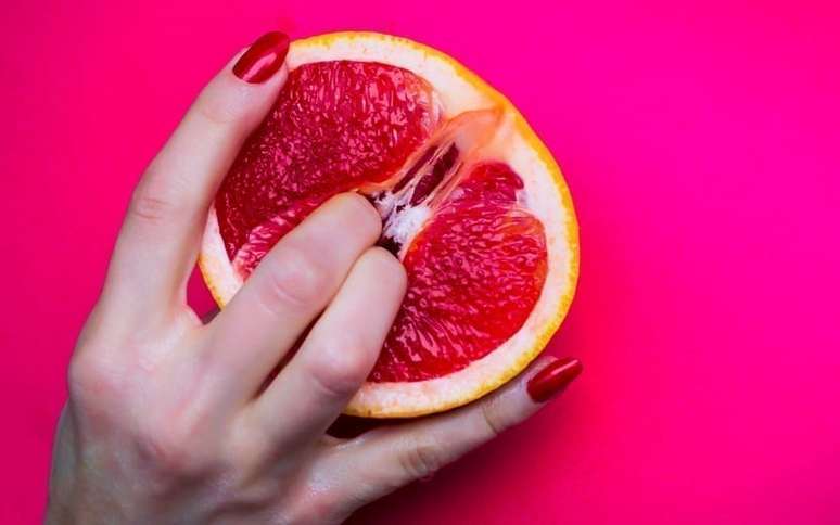 Mulher com os dedos dentro de uma laranja