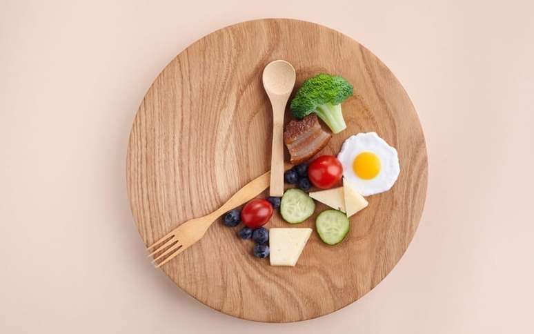 Prato de comida com talheres imitando ponteiros de um relógio e comidas em uma parcela dele