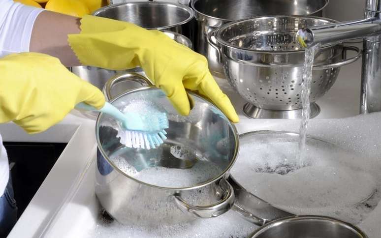 Pessoa limpando uma panela com esfreg&atilde;o e outras ao fundo