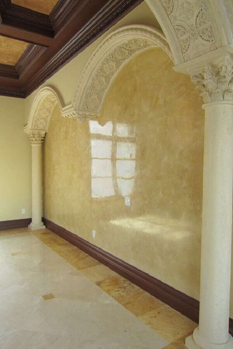55- A parede com textura em marmorato complementa a arquitetura com arcos de gesso e forro com madeiras aparentes. Fonte: Splat Paint