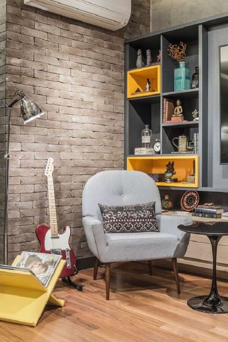 43. Poltrona decorativa cinza para sala com parede de tijolinho e estante de nichos planejada – Foto: Casa de Valentina