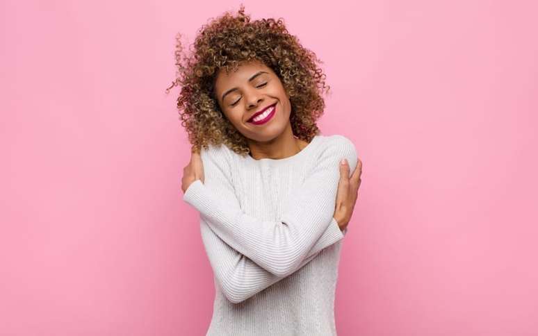 Mulher se abraçando em um fundo rosa