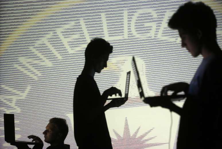 Silhueta de pessoas enquanto usam laptops em frente a uma imagem com códigos binários da Central Inteligence Agency (CIA). 29/10/2014.     REUTERS/Dado Ruvic 