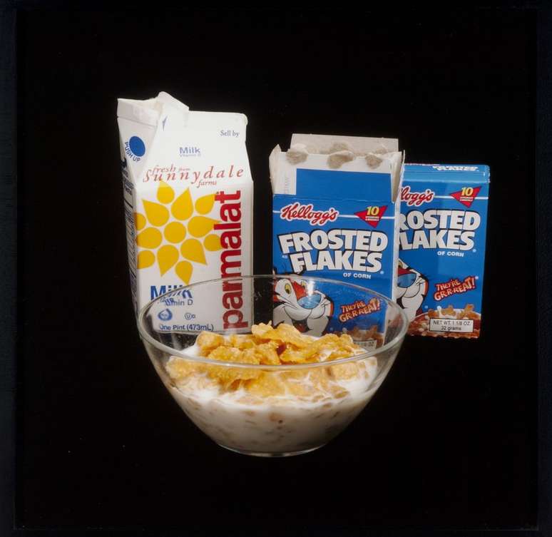 Uma tigela de cereal com leite, uma caixa de leite e dois pacotes de Sucrilhos.