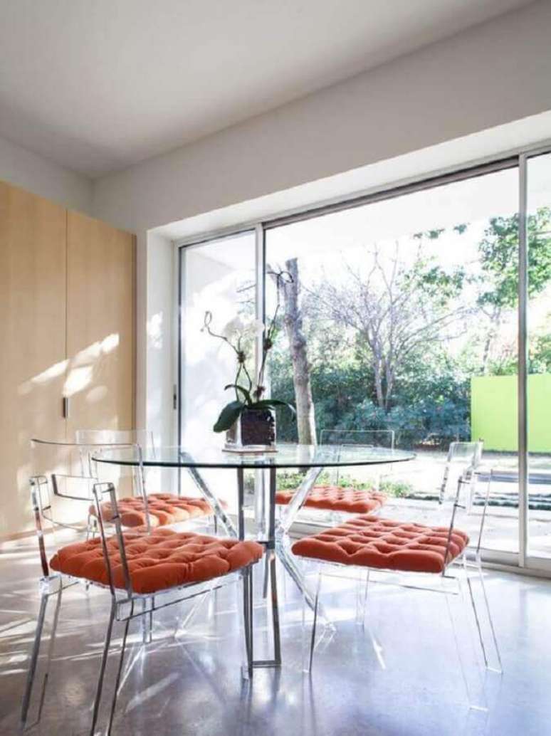 10. Decoração clean para sala de jantar com mesa de vidro redonda e cadeira de acrílico transparente com estofado laranja – Foto: Houzz