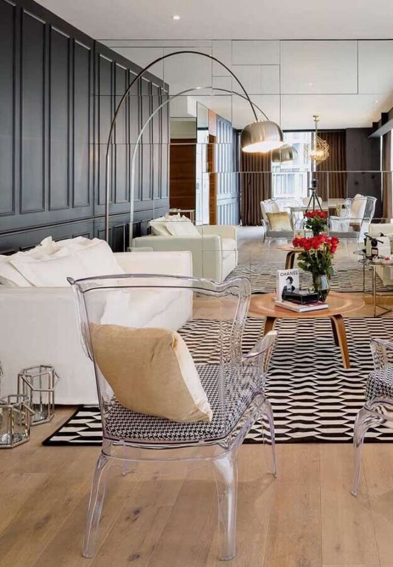 24. Sala sofisticada decorada com tapete preto e branco, parede espelhada e cadeira transparente com braço – Foto: Constance Zahn