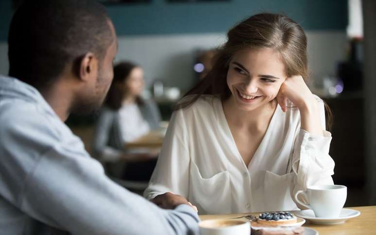 Moça sorrindo e paquerando um rapaz que está de costas