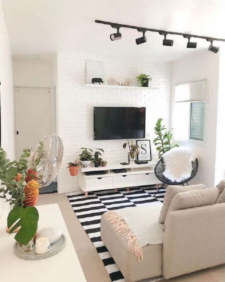 12. Decoração de sala branca com TV direto na parede de tijolinho e tapete listrado – Foto: Casa de Valentina