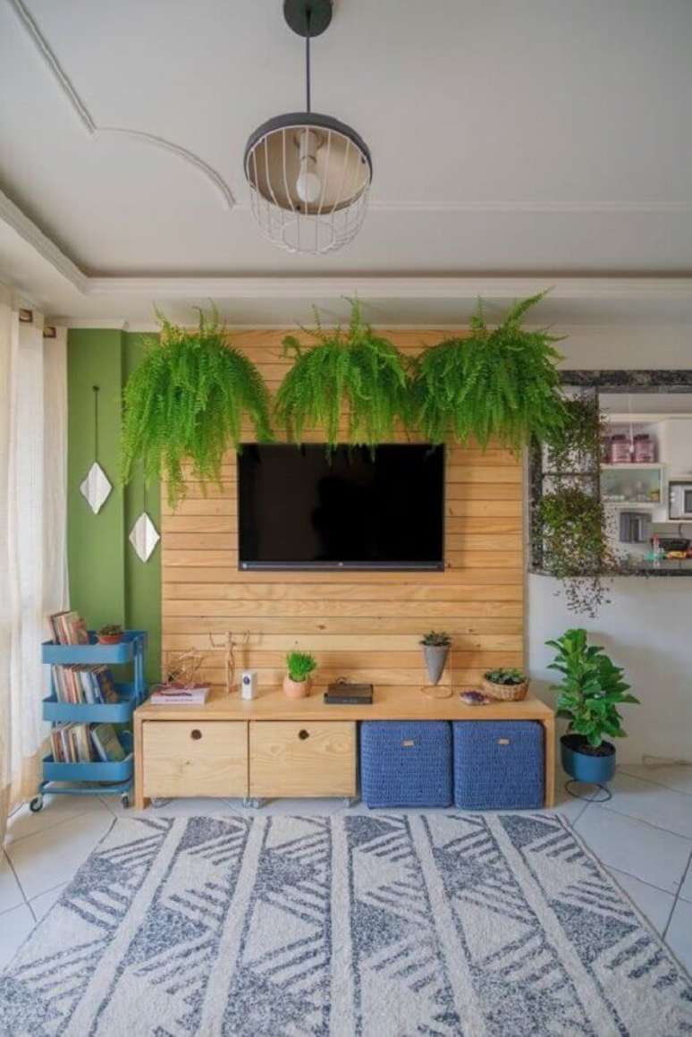 26. TV na parede decoração de sala com revestimento de madeira e samambaias suspensas – Foto: Diycore